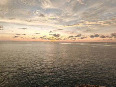 Gün batımında sakin bir okyanus manzarası. Suya yansıyan altın ışık ve gökyüzündeki dağınık bulutlar.