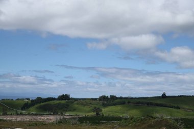 Güneşli kırsal yamaçlar sürüklenen bulutların altında uzanır.