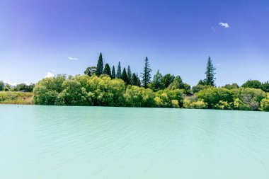 Calm water reflects vibrant foliage under clear sky shoreline ripples surface