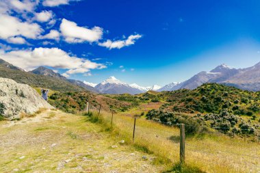 Uzak dağlık arazi manzarasının tadını çıkaran kişi, gezgin güneş ışığı altında sırt çantasıyla gezer.