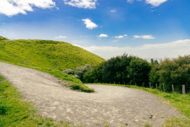 Güneşli kırsal patika, canlı yamaç manzarası yakınında rüzgarlar esiyor.
