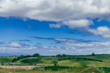 Huzurlu kırsal arazi, parlak bulutların altında uzanır.