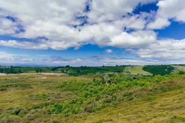 Uçsuz bucaksız kırsal alan, parlak bulutlu otlakların altında uzanır.
