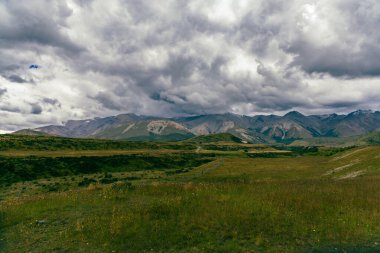 Uzak engebeli tepelerin üzerinde karanlık hava karamsar dramatik bulutlar sarıyor.