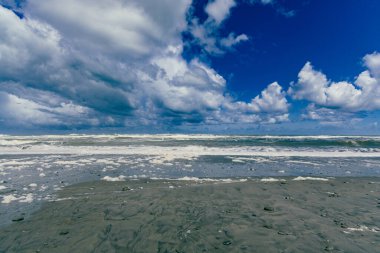 Köpüklü dalgalar, fırtınalı kümülüs kıyı şeridine çarpar.