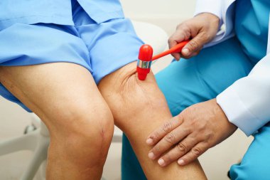 Asyalı doktor, hastanedeki yaşlı hastayı muayene etmek için diz refleksi sinirine vurdu..