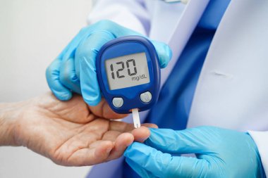 Diyabet tedavisinde kan şekeri seviyesini kontrol etmek için dijital glikoz ölçer kullanan Asyalı doktor.