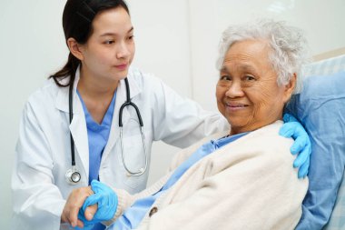 Asyalı doktor yaşlı kadın hasta sağlığını hastanede kontrol edip tedavi ediyor.