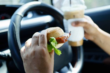 Asyalı kadın sürücü arabada hamburger yiyerek bekliyor..