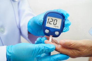 Diyabet tedavisinde kan şekeri seviyesini kontrol etmek için dijital glikoz ölçer kullanan Asyalı doktor.