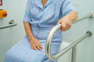 Asyalı yaşlı kadın hasta tuvalette tuvalet desteği kullanıyor..