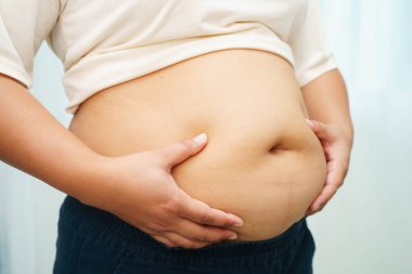 Asyalı kadın şişman göbeğini sıkmak için elini kullanıyor. Büyük boy aşırı kilolu ve obez..