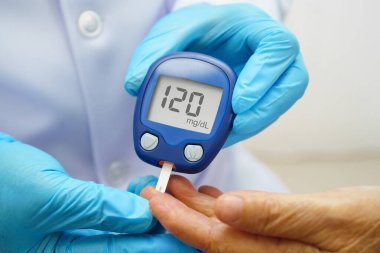 Diyabet tedavisinde kan şekeri seviyesini kontrol etmek için dijital glikoz ölçer kullanan Asyalı doktor.