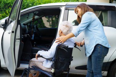 Bakıcı, Asyalı yaşlı kadın maluliyet hastasına arabaya binmek için tekerlekli sandalye kullanmasında yardım ediyor..