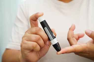 Evde parmak üzerinde dijital mızrakla kan şekeri seviyesini ölçmek için Asyalı kadın kendini test ediyor..