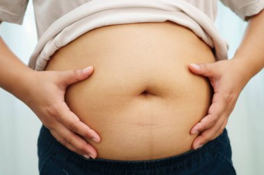 Asyalı kadın şişman göbeğini sıkmak için elini kullanıyor. Büyük boy aşırı kilolu ve obez..