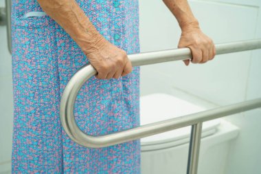 Asyalı yaşlı kadın hasta tuvalette tuvalet desteği kullanıyor..