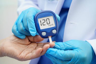 Diyabet tedavisinde kan şekeri seviyesini kontrol etmek için dijital glikoz ölçer kullanan Asyalı doktor.