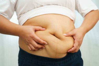 Asyalı kadın şişman göbeğini sıkmak için elini kullanıyor. Büyük boy aşırı kilolu ve obez..