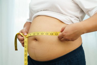 Asyalı kadın şişman göbeğini sıkmak için elini kullanıyor. Büyük boy aşırı kilolu ve obez..