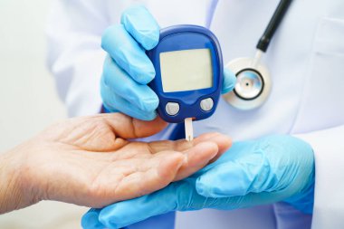 Diyabet tedavisinde kan şekeri seviyesini kontrol etmek için dijital glikoz ölçer kullanan Asyalı doktor.