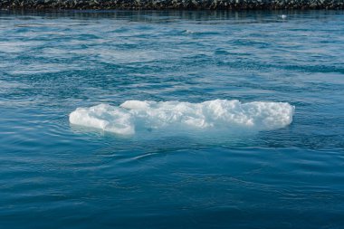 Okyanusta buzdağı, kayalık bir kıyıya sahip açık, güneşli, koyu mavi ve cyan tonlarıyla..