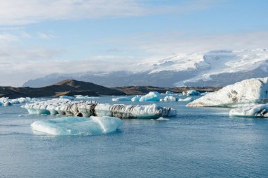 Açık bir günde arka planda karla kaplı dağların olduğu sakin bir buzdağının buzdağlarının manzarası..