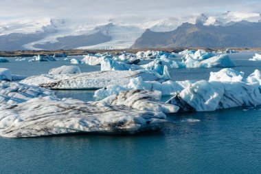 Buzdağları buzul sularında huzur içinde yüzer, uzak, karla kaplı dağlar görkemli bir zemin sağlar..