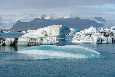 Farklı şekil ve boyutlarda çeşitli buzdağları bulutlu bir günde buzul gölünün mavi sularında yüzer..