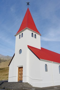 Mavi gökyüzünün altında gururla duran tuhaf beyaz bir kilise. Parlak kırmızı çatısı renklerle güzel bir kontrast oluşturuyor..