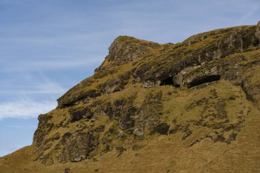 İzlanda dağında engebeli, kayalık bir arazi var. Yeşil çimenler bulutlu bir gökyüzünün altındaki yamaçları kaplar..