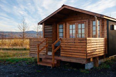 Kırsal bir ahşap kulübe, girişe doğru uzanan sakin bir tarlaya yerleştirilmiş rahat bir verandaya sahiptir..