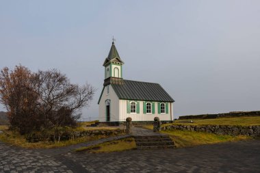 Yeşil süslemeli küçük, beyaz bir kilise huzur içinde duruyor. Bir kaldırım taşı yolu otlağın girişine götürür..