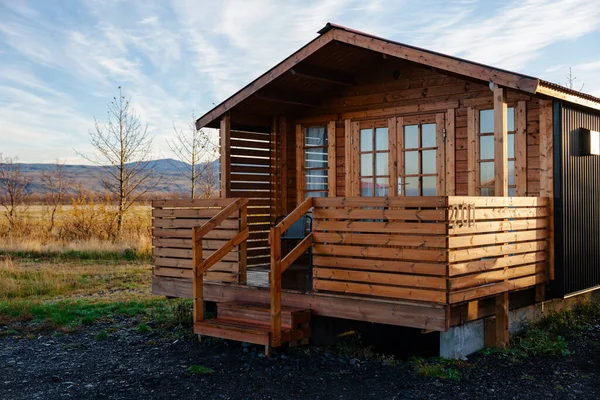 Kırsal bir ahşap kulübe, girişe doğru uzanan sakin bir tarlaya yerleştirilmiş rahat bir verandaya sahiptir..