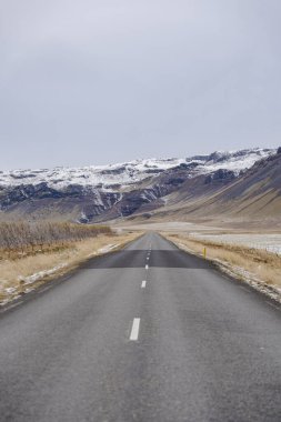Boş asfalt yollar kar kaplı dağlara götürür açık gri gökyüzü altında; sakin, seyahat, özgürlük, varış noktası