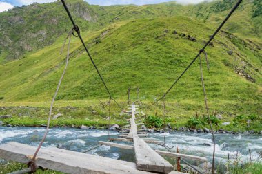 Yürüyüş yolunda güçlü akımla nehir üzerindeki asma köprü - macera, açık hava, doğa konsepti görüntüsü