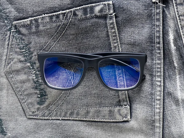 Vidro de sol de sombra azul na textura de jeans preto — Fotografia de Stock