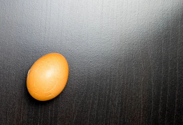 Розтріскування яйця на чорному блискучому фоні — стокове фото