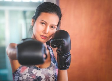 Asyalı bir kadın kapalı bir spor salonunda kameraya boks yumruğu atıyor spor yapıyor ve sağlıklı bir yaşam sürüyor..