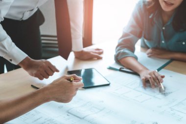 İnşaat mühendisi ve mimar inşaat planıyla birlikte çalışma masasında beyin fırtınası yapıyor.