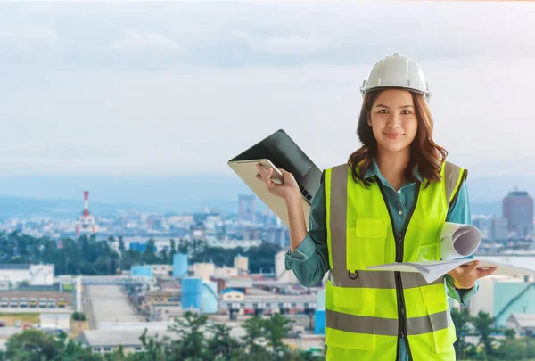 Female Civil engineer with computer and blueprint is standing infront Japan industry city in background.