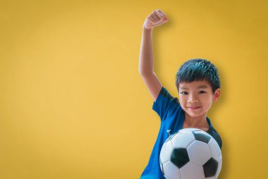 Küçük futbolcu çocuk sarı arka planda zafer eli gösteriyor..