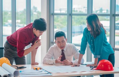 İnşaat Patronu ve mühendis ve mimar inşaat planıyla çalışma masasını tartışıyor.