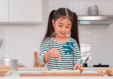 Asyalı kız hamuru yoğurmak ve mutfakta fırın hazırlamak için parmağını kullanarak eğleniyor..