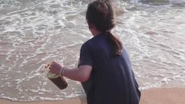 Çevre kirliliği konsepti için plajdan plastik çöpleri toplayan küçük bir kız..