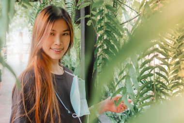 Güzel Asyalı genç dişi bitki yapraklarıyla dolu bir bahçede gülümsüyor..