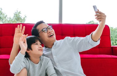 Asyalı baba ve oğul karantina döneminde video görüşmesi yaparken cep telefonlarına el sallıyorlar..