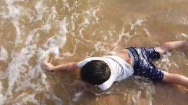 Küçük çocuk sahildeki dalgalardan plastik çöpleri topluyor.