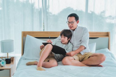 Baba ve oğul yatakta oturup ödev yapıyor bir kitap yazıyor, baba oğluna gülümseyerek yazmayı öğretiyor..