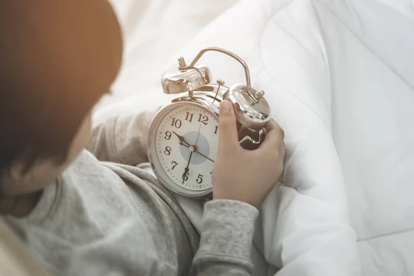 少年はベッドで目を覚ますと朝の遅い目覚まし時計を見て — ストック写真